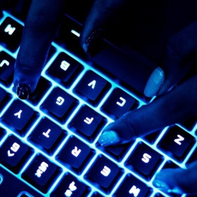 Uma fotografia de mãos femininas utilizando um teclado com led azul.